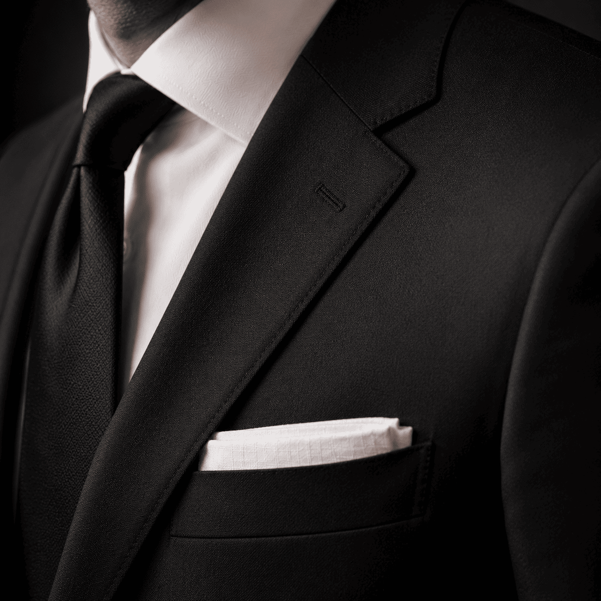 Close-up of a tailored black business suit featuring a crisp white dress shirt, black silk tie, notch lapel, and white pocket square, highlighting premium tailoring and luxury menswear craftsmanship.