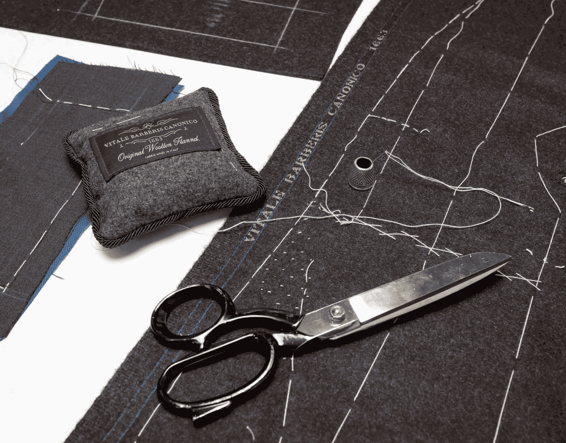 Custom fabrics, tailoring tools, and sewing patterns on a designer's workspace, representing Bold Italia Suit's affordable luxury tailoring by Vitale Barberis Canico.