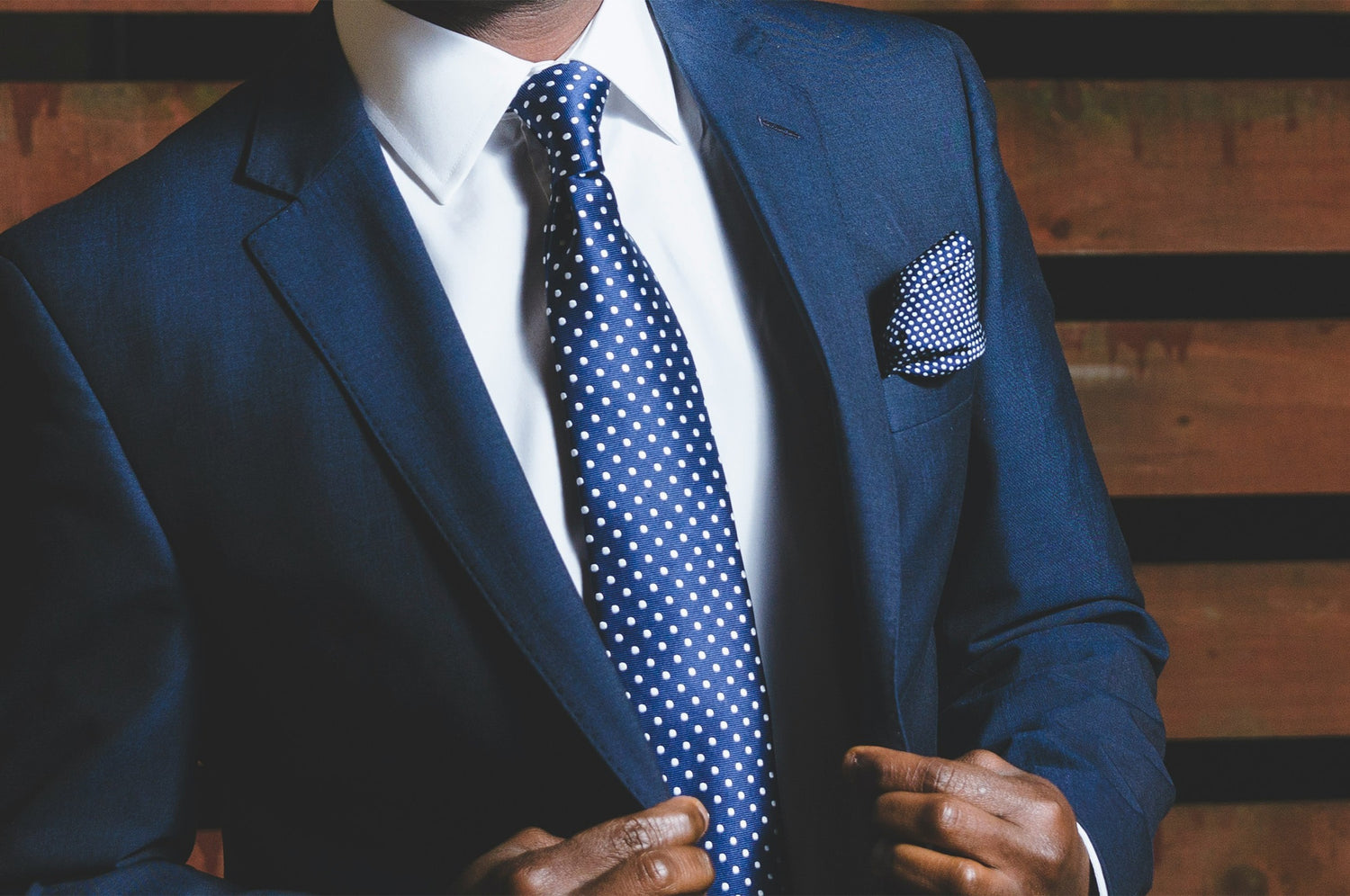 Man wearing a tailored navy blue suit with a white dress shirt, polka dot tie, and matching pocket square, representing Bold Italia Suit's luxury custom tailoring services.