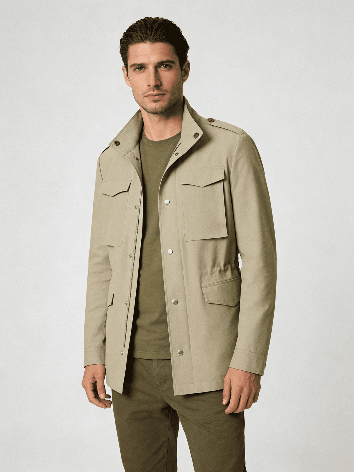 Man wearing a beige field jacket over an olive green shirt and pants on a white background