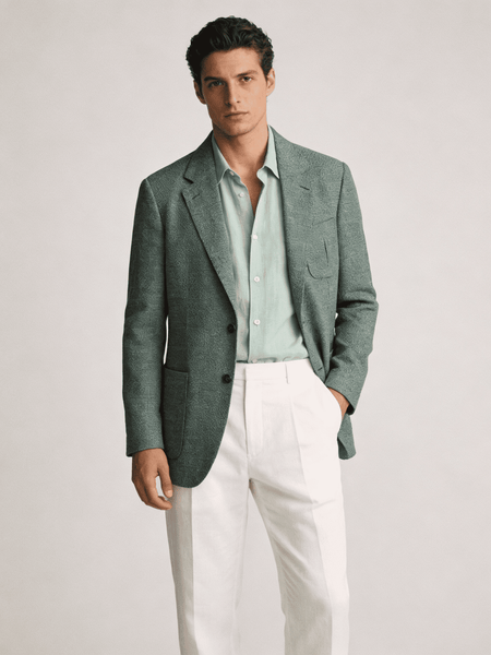 Man wearing a green blazer over a light shirt with white pants on a plain background