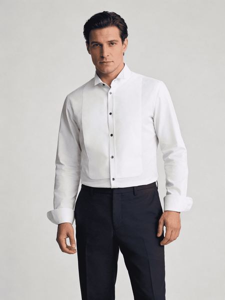 Man wearing a white dress shirt with black buttons and dark pants on a light gray background