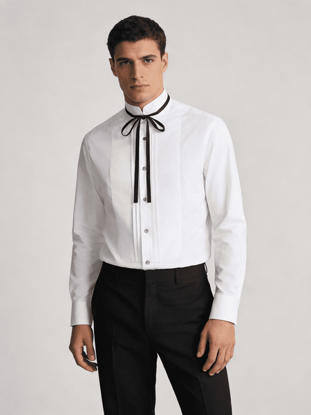 Man wearing a white dress shirt with a black bow tie and black pants on a light gray background