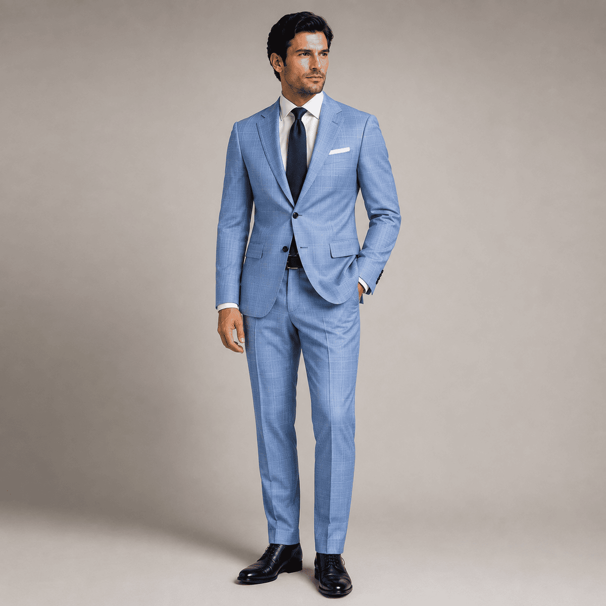 Full-body view of a man wearing a tailored light blue business suit with a crisp white dress shirt, navy silk tie, white pocket square, and polished black Oxford shoes, showcasing premium custom tailoring and luxury men's formalwear.