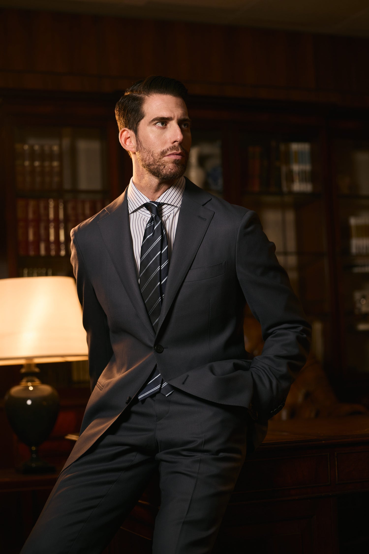 man wearing dark grey suit with striped shirt and tie formal business attire elegant office setting
