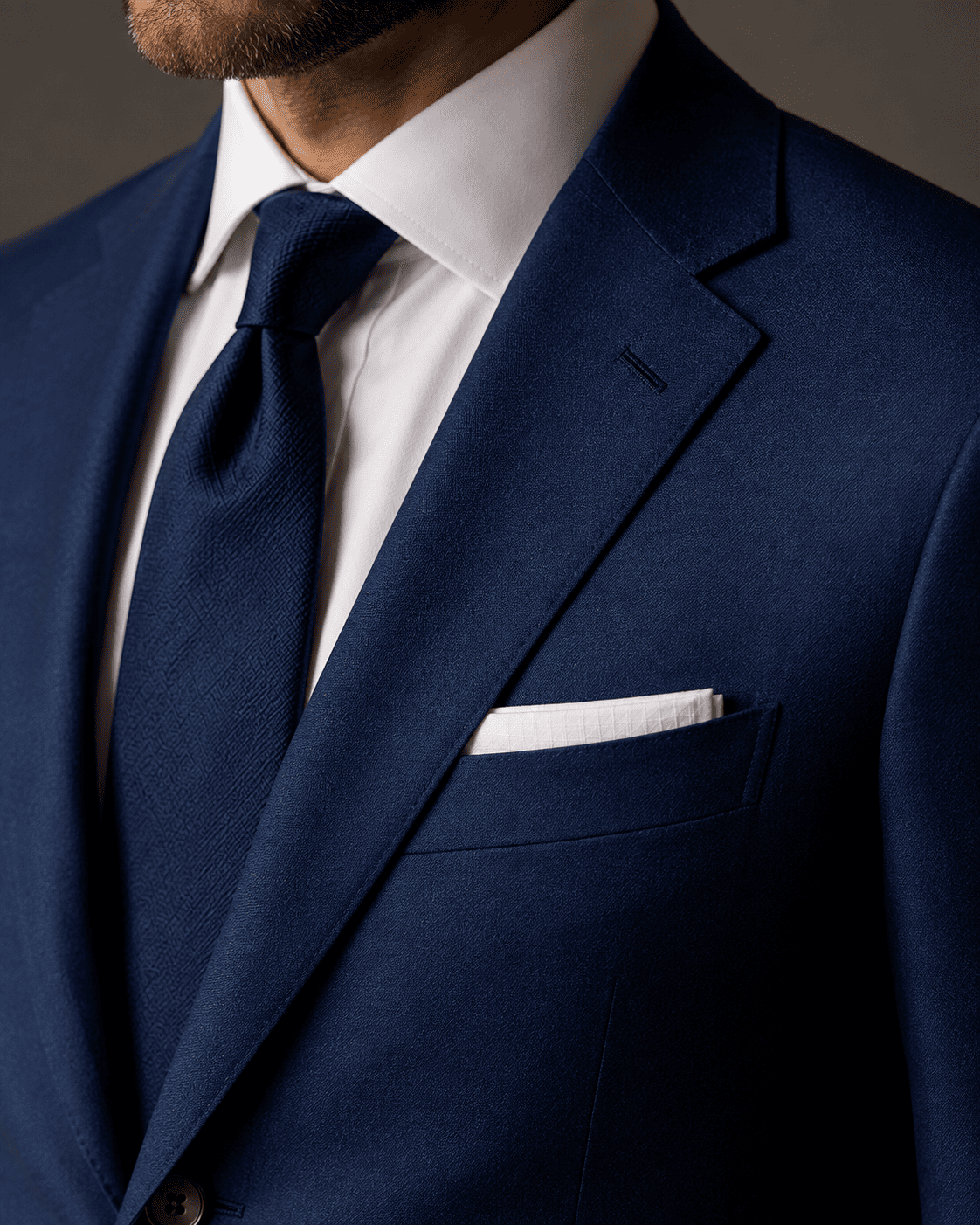 Close-up of a tailored navy business suit featuring a notch lapel, crisp white dress shirt, textured navy tie, white pocket square, and premium luxury men's tailoring.